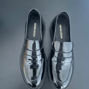 Svarta loafers från Agnes Cecilia - Snygga svarta loafers i lack från Agnes Cecilia. Dessa skor har en klassisk design med en elegant finish som passar perfekt för en stilren look. Perfekta för både vardag och mer uppklädda tillfällen.