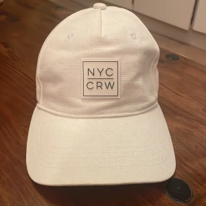 Vit keps - Snygg vit keps med broderad text 'NYC CRW' på framsidan. Perfekt för en stilren look. Justerbar passform. Jättebra skick.