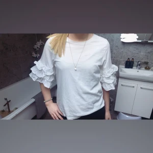Vit topp med volangärmar - Säljer en stilren vit topp med unika volangärmar. Perfekt för att ge en extra touch till din outfit. Toppen har en normal passform och är tillverkad i ett mjukt material.använt typ 5 gånger men inga symtom av fläckar,tror ej tröjan finns kvar att köpa