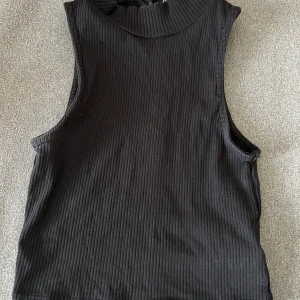 Svart ribbad ärmlös topp - Snygg svart ribbad topp med hög halsringning. 