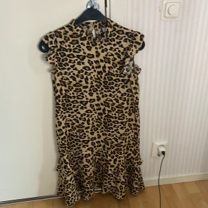 Leopardmönstrad klänning från Name It - Säljer en cool leopardmönstrad klänning från Name It. Klänningen har en volangdetalj vid fållen och är ärmlös, vilket ger en trendig look. Perfekt för den som vill sticka ut med ett djärvt mönster.