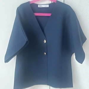 Mörkblå topp från Zara - Snygg mörkblå topp från  Zara med v-ringning och kortärmad design. Toppen har två guldknappar framtill som ger en elegant touch. Perfekt för en stilren look. Finns inte längre på Zara och toppen är i nyskick därav priset🥰
