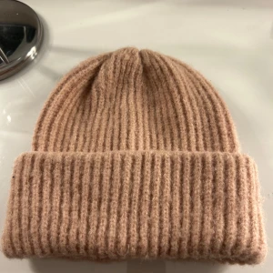 Beige ribbad mössa från Glitter - Säljer en mysig beige ribbad mössa från Glitter. Perfekt för kyliga dagar med sin mjuka och varma design. Mössan har en klassisk uppvikt kant som ger en stilren look. Sällan använd, max 3 gånger!💞