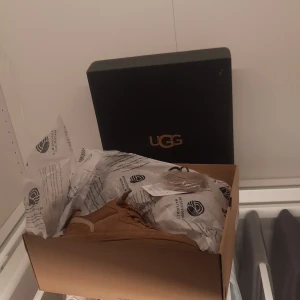 Bruna sneakers från UGG - Säljer ett par helt nya bruna sneakers från UGG med snörning och en bekväm design. Skorna har en robust sula och är tillverkade i mocka, vilket ger en stilren look. Perfekta för en avslappnad stil.nypris är 3300