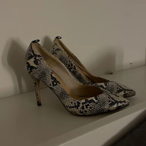 Klackskor  från H&M - Snygga pumps från H&M med ormskinnsmönster i svart och beige. Skorna har en spetsig tå och en elegant klack, perfekta för att ge en trendig touch till din outfit.