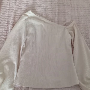 Vit offshoulder topp från NA-KD - Säljer en stilren off white offshoulder topp från NA-KD. Toppen har långa ärmar och är tillverkad i ett ribbat material som ger en snygg textur. Nästintill oanvänd. 
