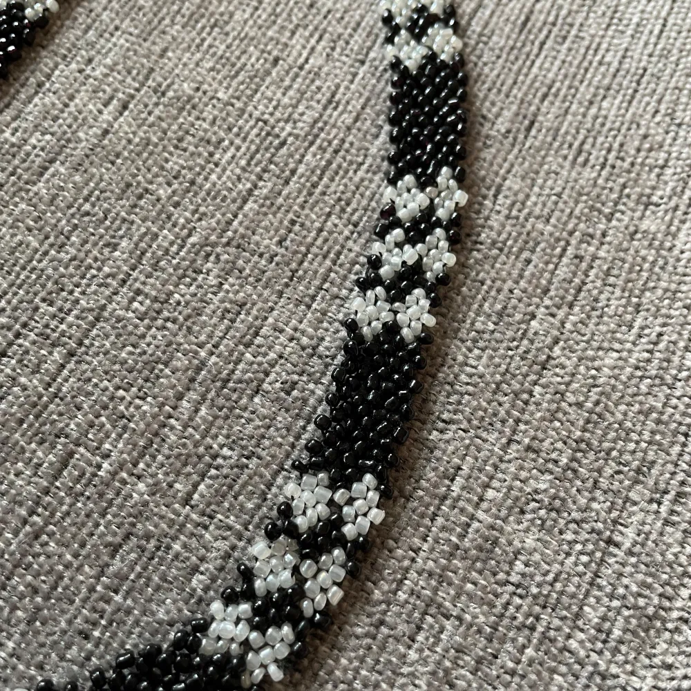 Unikt handgjort halsband med ett vackert mönster av svarta och vita pärlor. Halsbandet har ett blommigt mönster som ger en elegant touch. Perfekt för att lyfta vilken outfit som helst. Aldrig använt.. Asusteet.