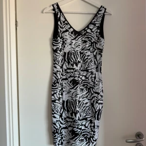 Svartvit klänning från ONLY - Snygg svartvit klänning från ONLY med ett zebramönster och v-ringad design. Klänningen är ärmlös och har en figurnära passform som framhäver silhuetten. Perfekt för en stilren look.