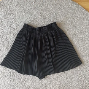 Svart plisserad kjol - Snygg svart plisserad kjol med elastisk midja. Perfekt för en stilren look. Kjolen har en luftig passform och är lätt att matcha med olika toppar.