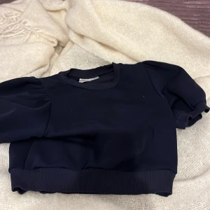 Svart tröja från Gina Tricot - Säljer en stilren svart tröja från Gina Tricot. Tröjan har korta puffärmar och en ribbad nederkant som ger en snygg passform. Perfekt för en trendig look!