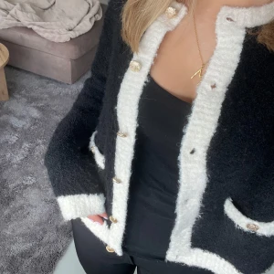 Svart och vit kofta från Holly & Whyte - Snygg och mysig svart kofta med vita detaljer från Holly & Whyte. Koftan har långa ärmar och knappar framtill. 