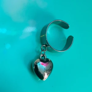 By prisförslag- Silverfärgad ring med hängande hjärta - Trendig silverfärgad ring med ett hängande hjärta. Perfekt för att ge en extra touch till din stil. Ringen är justerbar och passar de flesta storlekar.