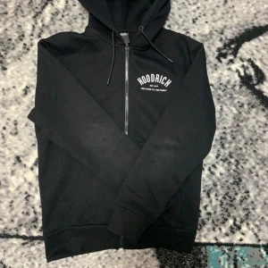 Svart hoodie från Hoodrich - Säljer en svart hoodie från Hoodrich med vit text 'Welcome to the family' på bröstet och ryggen. Tröjan har dragkedja och en klassisk huva med snören. Perfekt för en casual look.