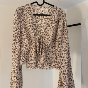 Beige Blus  - Blommig beige blus med utsvängda armar,  använd endast en gång. Knytdetalj på framsidan. Väldigt luftig och skön till sommaren🌸