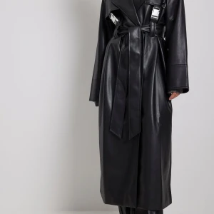 Svart skinn trenchcoat med silver ditaljer - Snygg svart trenchcoat i skinn med långa ärmar och ett bälte i midjan. Jackan har en klassisk krage och stilrena detaljer som ger en cool look. Perfekt för att höja din stil till nästa nivå. Helt ny köptes för två år sen 💞💞