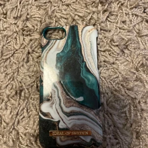 Iphone 6 Mobilskal från iDeal of Sweden - Snyggt mobilskal från iDeal of Sweden med ett marmorerat mönster i gröna och vita nyanser. Skalet har en elegant design med en guldig logotypdetalj. Perfekt för att ge din telefon ett stilrent utseende.