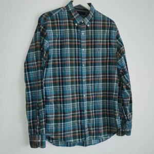 Rutig skjorta från Tommy Hilfiger - Snygg rutig skjorta från Tommy Hilfiger i blå, grön och orange. Skjortan har långa ärmar och knappar framtill. Perfekt för en stilren look.