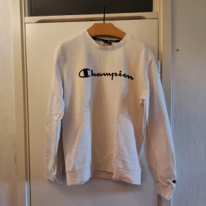 Vit sweatshirt från Champion - Säljer en klassisk vit sweatshirt från Champion med deras ikoniska logga broderad på bröstet. Tröjan har långa ärmar och en bekväm passform, perfekt för en avslappnad stil. 🏆St M, tecken på användning