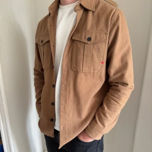 Brun overshirt från R.D.D. - Säljer en nice brun overshirt från R.D.D med deras röda signaturmärke. Perfekt för den kommande våren. Den är köpt på Jack & Jones och är i stort sett i nyskick. Storlek M. 