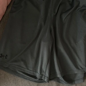 Grå träningsshorts från Under Armour - Snygga gråa träningsshorts från Under Armour i ett lätt och luftigt syntetmaterial. 