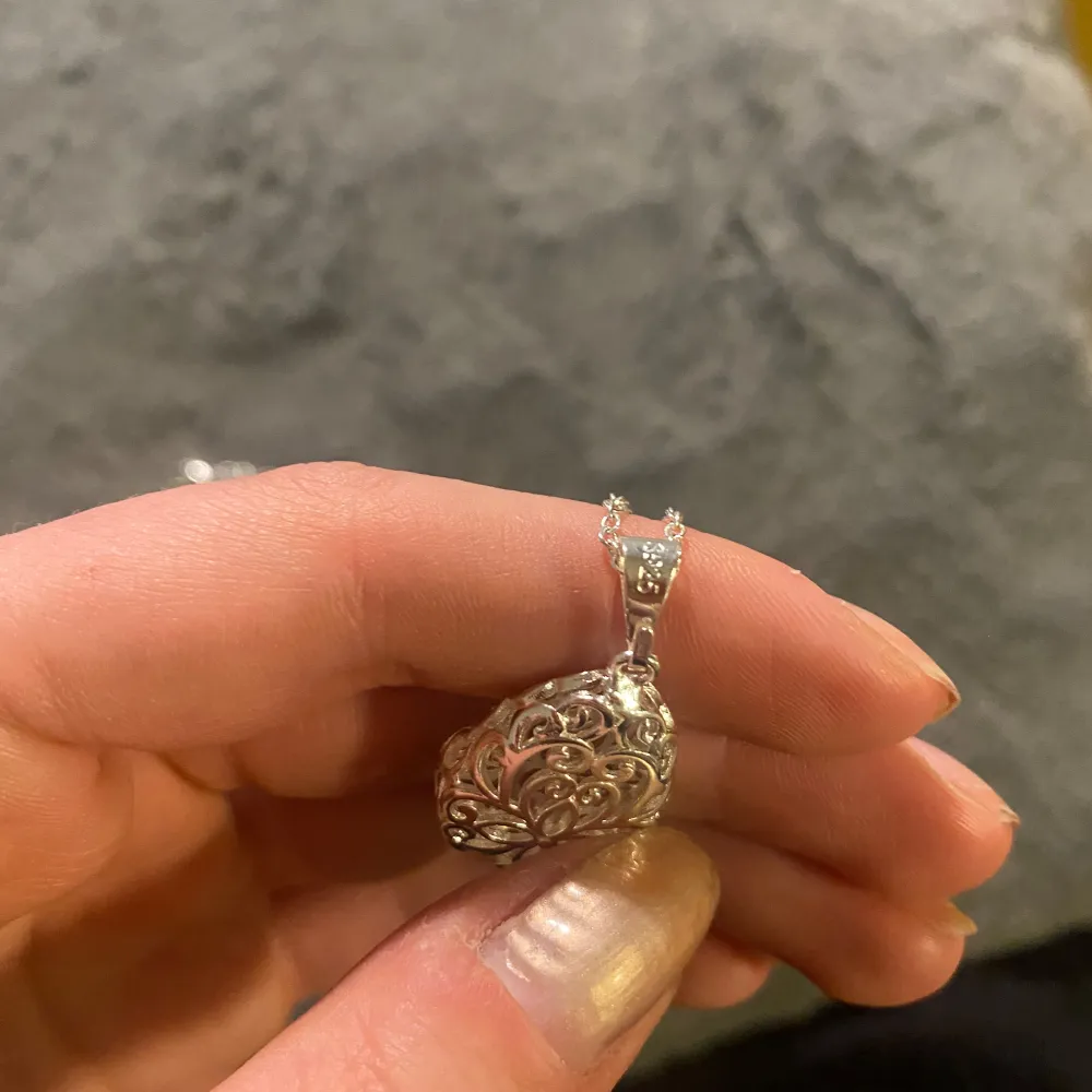 Elegant silverfärgat halsband med ett detaljerat, droppformat hänge. Hänget har ett vackert utskuret mönster som ger en stilren och sofistikerad look. Kedjan är tunn och smidig med ett enkelt lås för säker användning. Silver 925. Helt ny . Asusteet.