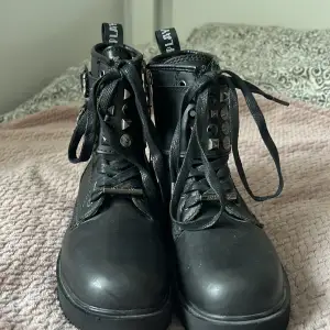 Säljer ett par svarta boots från Replay i nyskick. De är gjorda av polyster och har coola detaljer som nitar och snörning. Bootsens sula är robust och mönstrad för bra grepp. Perfekta för höst och vinter!