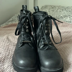 Svarta boots med nitar från Replay - Säljer ett par svarta boots från Replay i nyskick. De är gjorda av polyster och har coola detaljer som nitar och snörning. Bootsens sula är robust och mönstrad för bra grepp. Perfekta för höst och vinter!