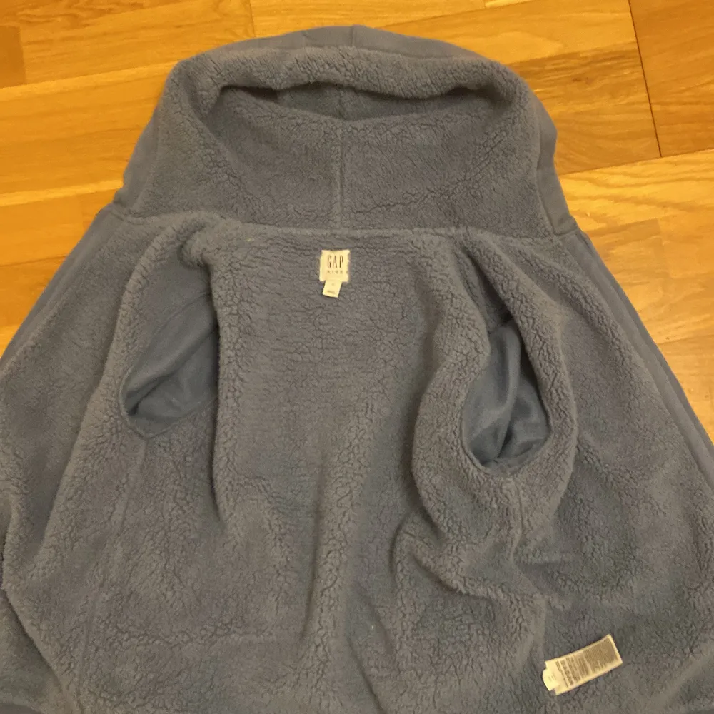 Säljer en supermysig blå hoodie från GAP. Den har en stor logga på framsidan och en dragkedja hela vägen ner. Insidan är fodrad med mjuk fleece, perfekt för kyliga dagar. Den har långa ärmar och en praktisk huva. Perfekt för både vardag och chill!. Tröjor & Koftor.