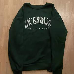 Mörkgrön sweatshirt med text: ”LOS ANGELES” california. Tröjan kommer ifrån Chain och är storlek M