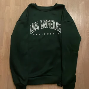 Mörkgrön sweatshirt🦎 - Mörkgrön sweatshirt med text: ”LOS ANGELES” california. Tröjan kommer ifrån Chain och är storlek M