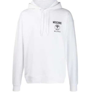 Vit hoodie från Moschino - Säljer en snygg och stilren vit hoodie från Moschino med deras ikoniska logga tryckt på bröstet. Den har en klassisk passform med långa ärmar och en bekväm huva med dragsko. Perfekt för en casual look eller att mysa i hemma. 🖤