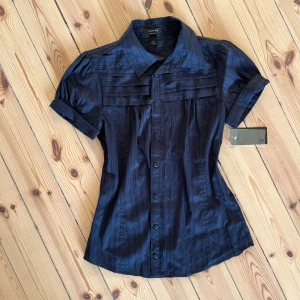Mörkblå blus med korta ärmar - Säljer en elegant mörkblå blus från mango. Den har korta ärmar och knappar framtill. Samt lite puffiga ärmar. Väldigt söt men tyvärr för liten för mig! Passar mer M