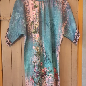 Blommig klänning från OOO - Säljer en superfin klänning från Uoozee med ett färgglatt blommönster. Klänningen har en härlig mix av blå och rosa nyanser med vackra blommor i rött och rosa. Den har korta ärmar och en lös passform, lite asianperfekt för fest eller en dag på stan. 