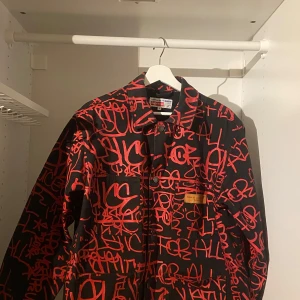 Svart och röd jacka från Supreme x Comme des Garçons - Säljer en unik svart jacka med rött graffiti-mönster från Supreme x Comme des Garçons. 