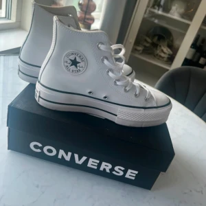 Chuck Taylor all star lift- höga sneakers vita - Säljer ett par klassiska vita Converse All Star sneakers i hög modell. Skorna har snörning och den ikoniska logotypen på sidan. Perfekta för en stilren och avslappnad look.