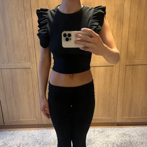 Svart croppad topp med volangärmar - Snygg svart croppad topp med volangdetaljer på axlarna. Perfekt för en trendig look.