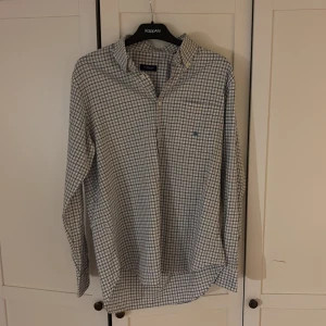Rutig skjorta från Burberry - Snygg rutig skjorta från Burberry i blått och vitt. Skjortan har långa ärmar och knappar framtill. Perfekt för en stilren look med klassisk design och broderad logga på bröstet.