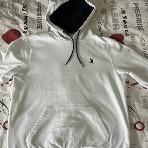 Vit hoodie från U.S. Polo Assn. - Säljer en stilren vit hoodie från U.S. Polo Assn. med en liten logga på bröstet. Den har en praktisk magficka och justerbar huva med snören. Perfekt för en avslappnad stil. Rekommenderad för storlek S eftersom Hoodien är liten för sin storlek. 