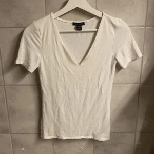 Vit v-ringad topp från Amisu - Säljer en stilren vit v-ringad topp från Amisu. Toppen har korta ärmar och är tillverkad i ett mjukt material som ger en skön passform. Perfekt för en enkel och fräsch look. Toppen sitter ganska tajt och ger en fin figur.