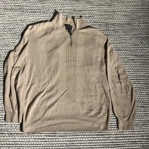 Beige tröja med dragkedja från H&M - Säljer en stilren beige tröja med dragkedja och ribbade detaljer. Perfekt för en avslappnad look med långärmad design och hög krage.