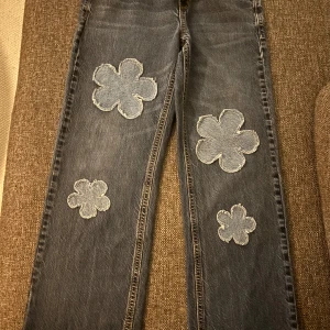 Blå jeans med blommiga detaljer från Old Navy - Snygga blå jeans från Old Navy med unika blommiga detaljer. De har en straight fit och är perfekta för en avslappnad stil. Blommorna ger en lekfull touch till den klassiska jeanslooken. Står stl M men mer som XS/S