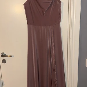 Långklänning i satin - Min balklänning för 2 år sedan Endast använd 1 gång Bra längd för mig med klackar, är 163 lång Sitter fint och har ett fint fall av tyg vid bysten Knappar och dragkedja i bak, dock har en knapp lossat i bak, men har den sparad så den kan man lätt sy på