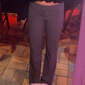 Grå byxor med unik midjedetalj - Snygga grå byxor med en speciell omlottdetalj vid midjan. De har en tight passform och är perfekta för en stilren look. Byxorna är raka och ger en elegant siluett.