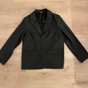 Svart kavaj och byxor - Snygg svart kavaj med matchande byxor. Kavajen har två knappar framtill och klassiska slag. Byxorna har en rak passform med knapp och dragkedja i gylfen. Perfekt för formella tillfällen.