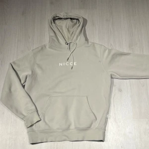 Beige hoodie från Nicce - Säljer en stilren beige hoodie från Nicce med justerbar huva och ficka. Perfekt för en avslappnad look. Den har långa ärmar och en bekväm passform. Storlek M