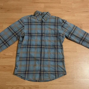 Rutig skjorta från Eddie Bauer - Säljer en klassisk rutig skjorta från Eddie Bauer i blått och brunt. Skjortan har långa ärmar och knappar framtill. Perfekt för en avslappnad stil.