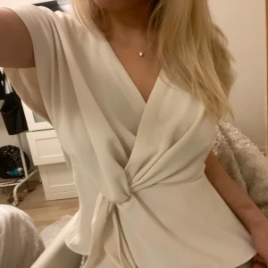 Vit ZARA omlottopp - Säljer en stilren vit omlottopp från Zara med korta ärmar och knytning i midjan. Perfekt för en elegant look. Passar bra till både jeans och kjol.