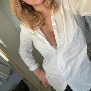 Vit skjorta - Säljer en klassisk vit skjorta med knappar framtill. Skjortan har långa ärmar och en normal passform