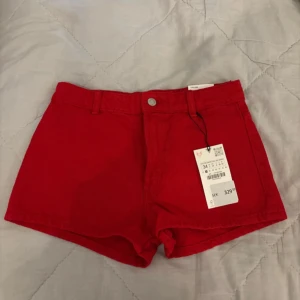 Röda shorts från Zara - Snygga röda shorts från Zara i en härlig färg. De har en knapp och dragkedja framtill samt hällor för bälte. Perfekta för sommardagar!