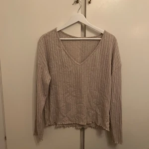 Beige ribbad tröja - Säljer en beige ribbad tröja med v-ringning och långa ärmar. Perfekt för en avslappnad stil. Tröjan har en lös passform och är tillverkad i ett mjukt material.
